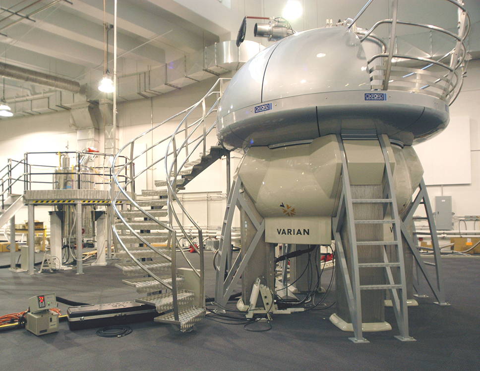 Photo of an NMR spectrometer, which looks like two large silver spheres, one on top of the other, with several sets of stairs leading to the top.