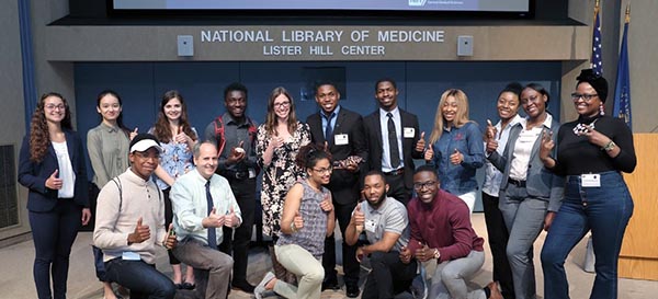 Melissa and Jon Lorsch posing on the lecture stage with eight female students and six male students.
