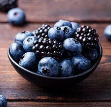 Blueberries and blackberries in a bowl and scattered on a wooden table.