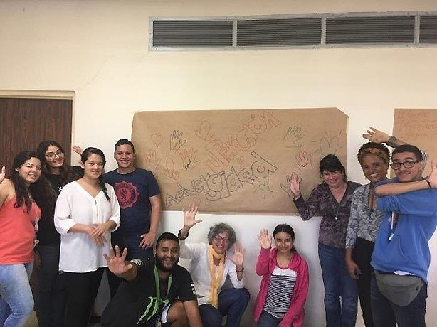 Dr. Ortiz standing with other standing and kneeling students in a classroom, smiling and waving.
