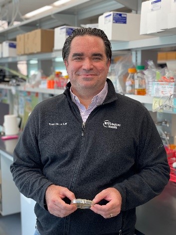 Dr. Torres standing in a lab holding a Petri dish.