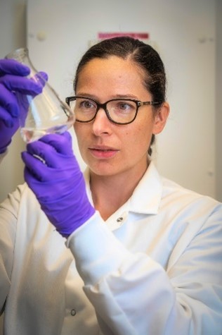 Dr. Boros wearing a lab coat and gloves and holding a flask.