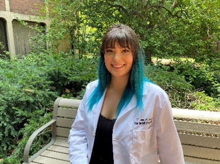 Christina Chavez wearing a lab coat and sitting on a park bench.