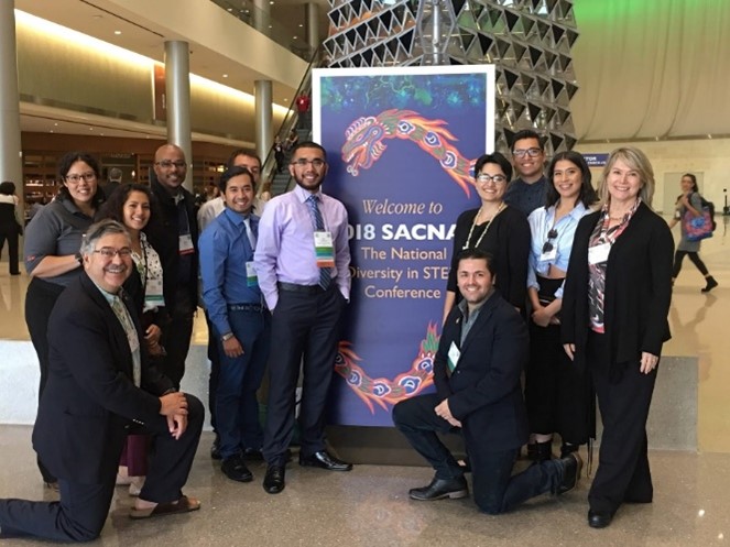 A group of twelve people posing for a picture in front of a conference welcome sign.
