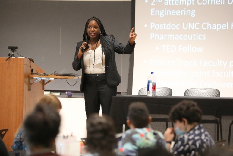 Dr. Wayne standing on stage and speaking into a handheld microphone during a live lecture.