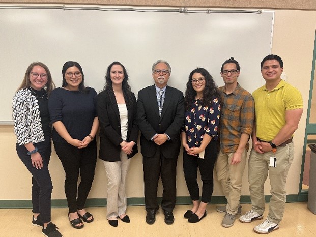Seven people standing in front of a whiteboard, including Claira, who's standing to the right of Dr. Romero.