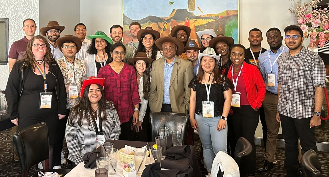 Dr. Badu-Tawiah surrounded by 21 other individuals at an indoor gathering.