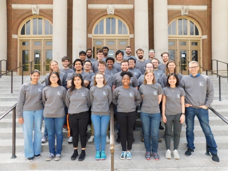 28 individuals standing on stairs leading up to a building.