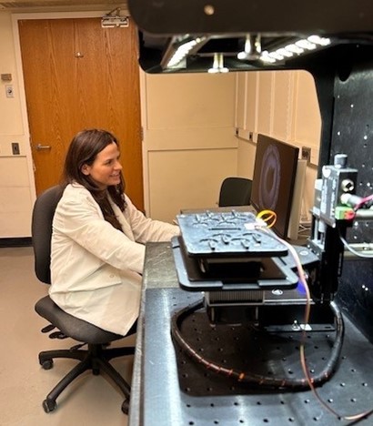 A scientific camera in the foreground and Dr. Palavicino-Maggio looking at a computer screen behind it.